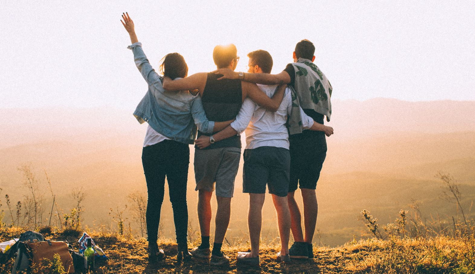 Four friends stand arm in arm at sunset, looking out at the hills