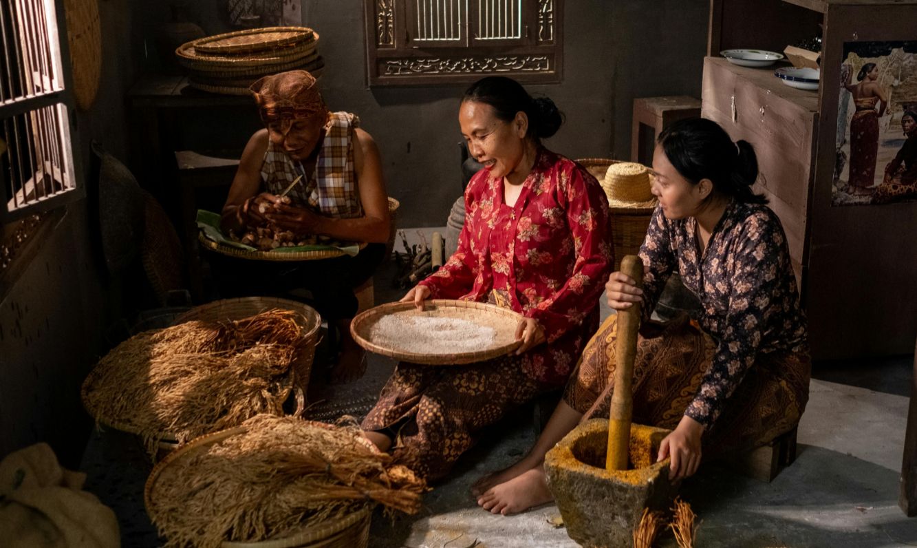 Three women sit together preparing rice in a quiet home